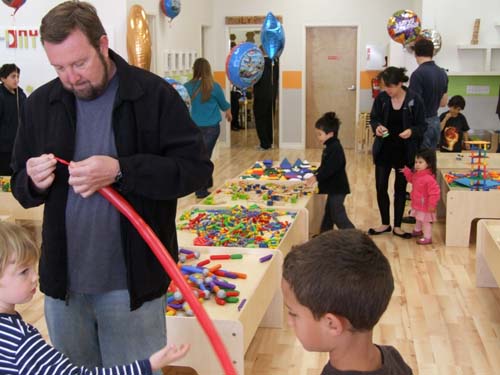 Parent Lon Woodard shapes a balloon as children in background avail themselves of regular activities at Built It-The Kid Workshop