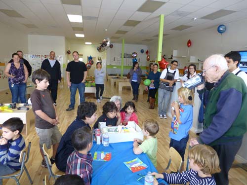 Sky Masori blows the candles on his birthday cake as he watched by his older brother Shor, grandma Nancy and cousin Sara.  In foreground great-grandpa Sam videos the occasion bringing together kindergarten classmates and their parents.