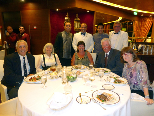 Ian Harkness (right, standing) takes advantage of his white dinner jacket to join wait staff in Rotterdam dining room.  Seated at table are from left, Donald and Nancy Harrison of San Diego; Debbie and Greg Clarke of Grandview Lake, Saskatchewan, and Barbara Hoskins of Newbury, England